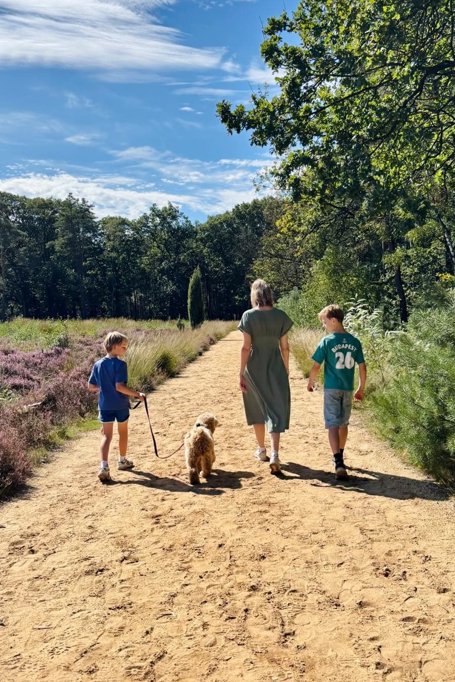 Yanieke wandelt met haar twee zoons en de hond over een zandpad door de heide.